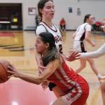 Wasilla junior Katie Jackson drives and passes around Juneau-Douglas High School: Yadaa.at Kalé seniors Cailynn Baxter and Addison Wilson (10) during the Warriors 65-34 win Friday over the Crimson Bears in the George Houston Gymnasium. (Klas Stolpe / Juneau Empire)