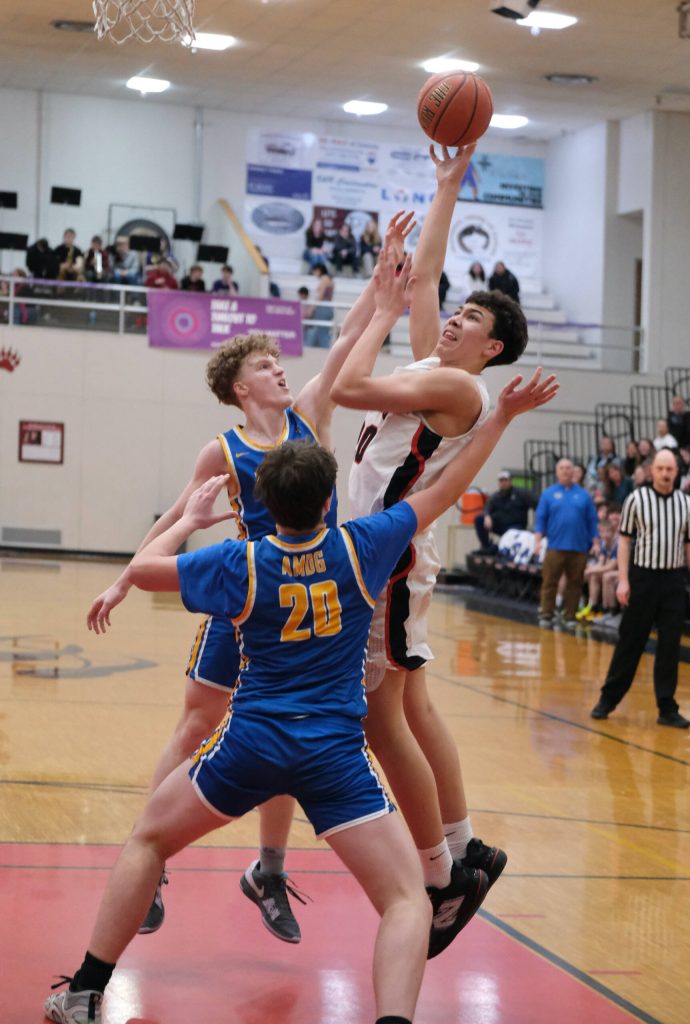 Juneau-Douglas High School: Yadaa.at Kalé junior Elias Dybdahl shoots over Monroe sophomore Zavier Oleson and junior James Trieglaff (20) during the Crimson Bears 76-55 loss to the Rams on Friday in the George Houston Gymnasium. (Klas Stolpe / Juneau Empire)