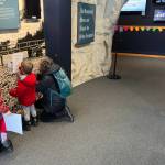 Matt Knutson (right) watches as his wife Rosary Lombardo helps their grandchildren Jasper Lombardo-Brown, 6, and Felix Lombardo-Brown, 3, with a snowflake scavenger hunt as part of the Mendenhall Minis event at the Mendenhall Glacier Visitor Center on Saturday morning. (Mark Sabbatini / Juneau Empire)