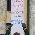 A protester holds up a sign that says cutting Medicaid is genocide on the American people on Wednesday, March 12, 2025. (Jasz Garrett / Juneau Empire)