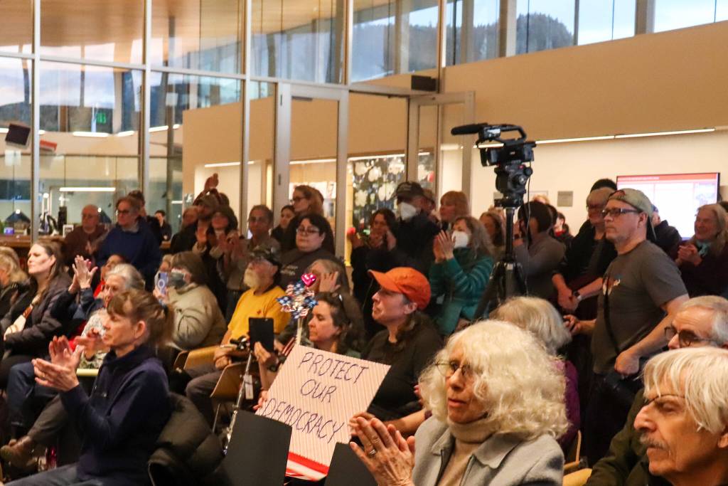 Attendees of an empty-chair town hall clap on Thursday, March 20, 2025. A Juneau resident holds a sign that says protect our democracy. (Jasz Garrett / Juneau Empire)