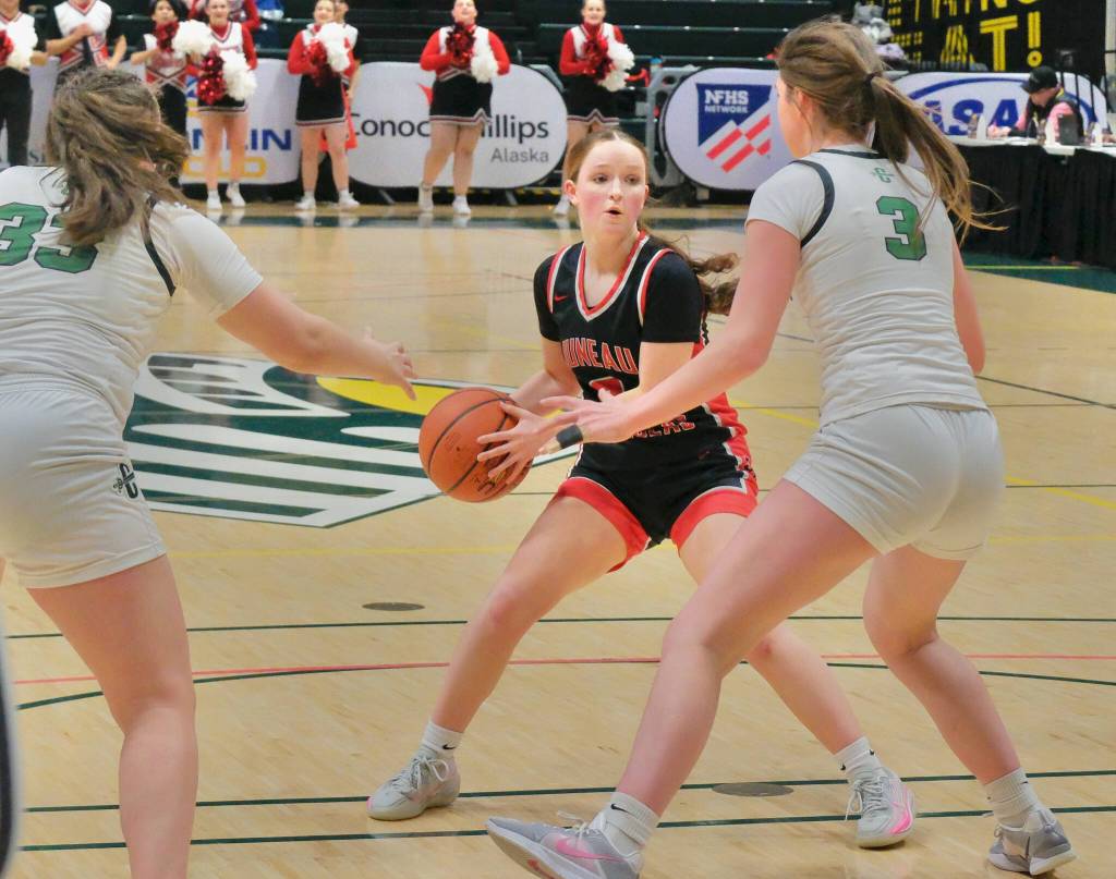 Juneau-Douglas High School: Yadaa.at Kalé junior Cambry Lockhart (3) looks to pass under pressure from Colony senior Tonya Karpow (33) and sophomore Jericho Wuestenberg (3) during the Crimson Bears 56-34 loss to the Knights in a Friday 4A girls semifinal at the 2025 ASAA March Madness Alaska 3A/4A Basketball State Championships at Anchorages Alaska Airlines Center. (Klas Stolpe / Juneau Empire)