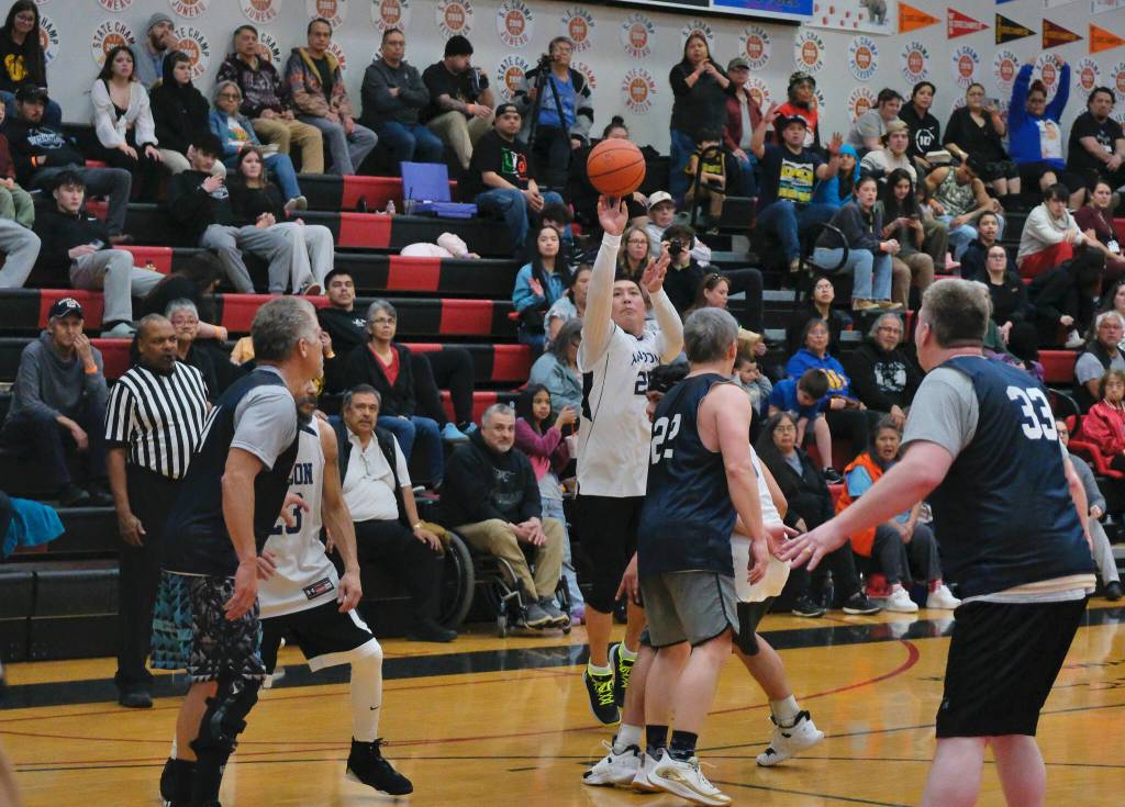 Angoons Kenny Willard Jr. (25 hits a shot past the arc over Metlakatlas Archie Dundas (22) during Metlakatlas 76-60 Masters Bracket elimination game win Wednesday at the 76th Annual Juneau Lions Club Gold Medal Basketball Tournament in Juneau-Douglas High School: Yadaa.at Kalés George Houston Gymnasium. (Klas Stolpe / Juneau Empire)