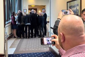 Visitors to the Alaska Capitol take pictures as members of the Houses Republican minority gather in a hallway to discuss an upcoming vote on Wednesday, Feb. 19, 2025. (James Brooks/Alaska Beacon)