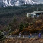 Tourists walk below a closed Mendenhall Glacier visitor center on Monday, April 14, 2025. (Jasz Garrett / Juneau Empire)