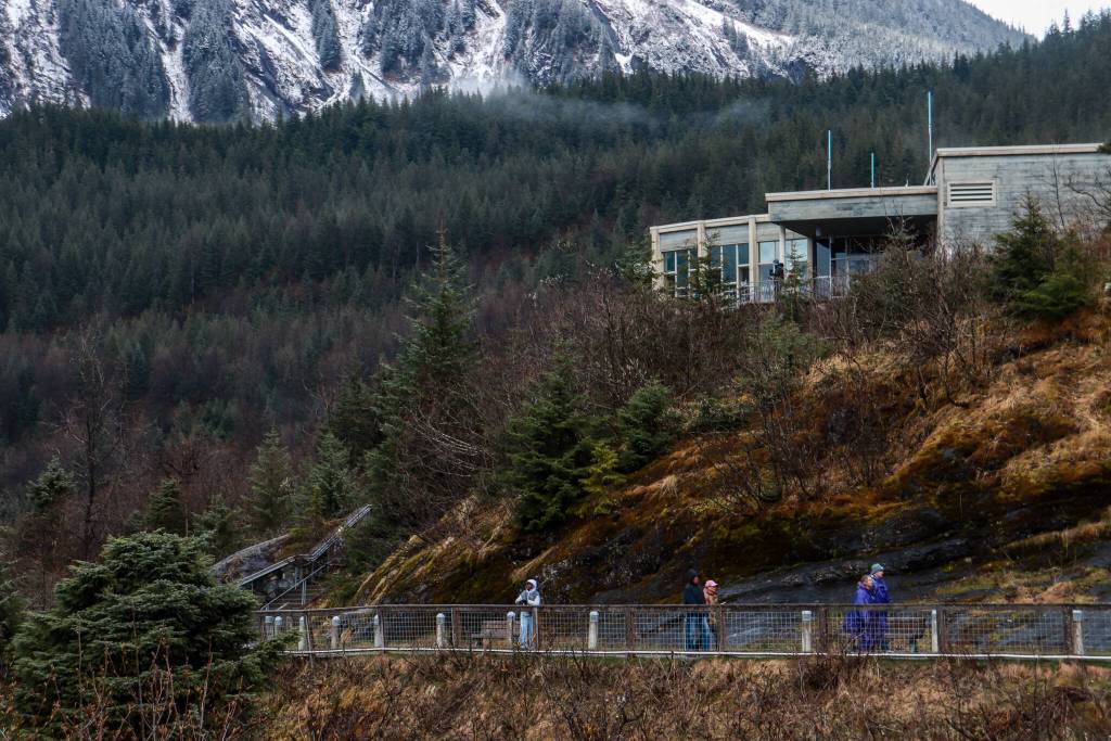 Tourists walk below a closed Mendenhall Glacier visitor center on Monday, April 14, 2025. (Jasz Garrett / Juneau Empire)