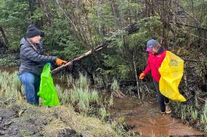 Tina Martin, left and her daughter, Isabelle, 17, clean trash from a stream along Back Loop Road on Saturday. (Mark Sabbatini / Juneau Empire)