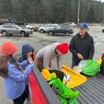 Randy Hurtte, right, hands out trash and recycling bags to James McFerran, his daughter Harper, 11, and son Calvin, 9, at Western Auto Marine on Saturday. (Mark Sabbatini / Juneau Empire)