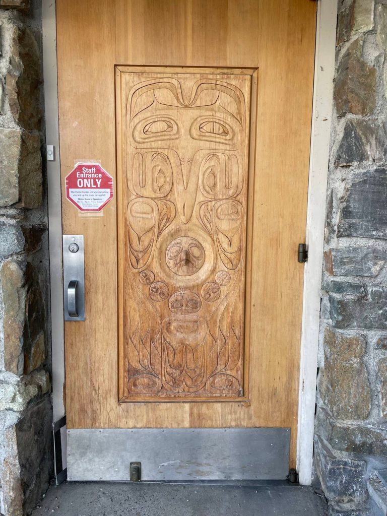 Original visitor entry door to the Mendenhall Glacier Visitor Center with totemic legend design carved in 1961 by architect Steve Forrest, son of lead architect Linn Forrest Sr. (Photo by Laurie Craig)