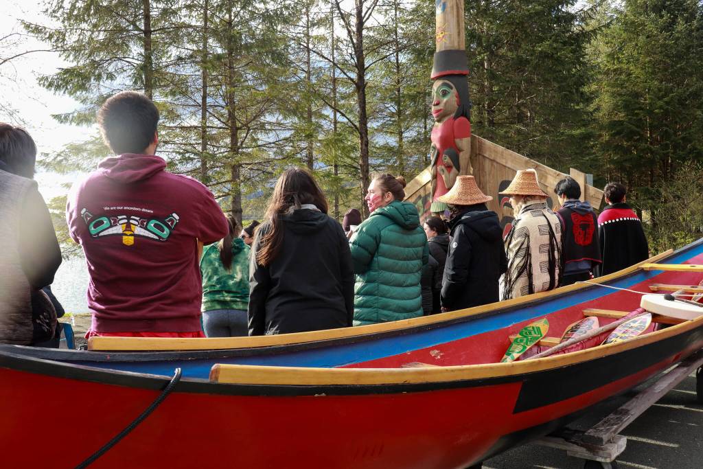People attend a Missing and Murdered Indigenous Persons Remembrance Ceremony at Twin Lakes on Monday, May 5, 2025. Two of Wayne Prices creations, a healing dugout canoe and totem pole, are seen together for the ceremony. (Jasz Garrett / Juneau Empire)