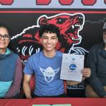 Juneau-Douglas High School: Yadaa.at Kalé senior Pedrin Saceda-Hurt signed an NCAA Division III student-athlete form on Wednesday in the JDHS commons to attend Luther College in Decorah, Iowa, and play for the Norse basketball team. At left is mother Nickie Saceda-Hurt and at right is father Frank Hurt. (Klas Stolpe/Juneau Empire)