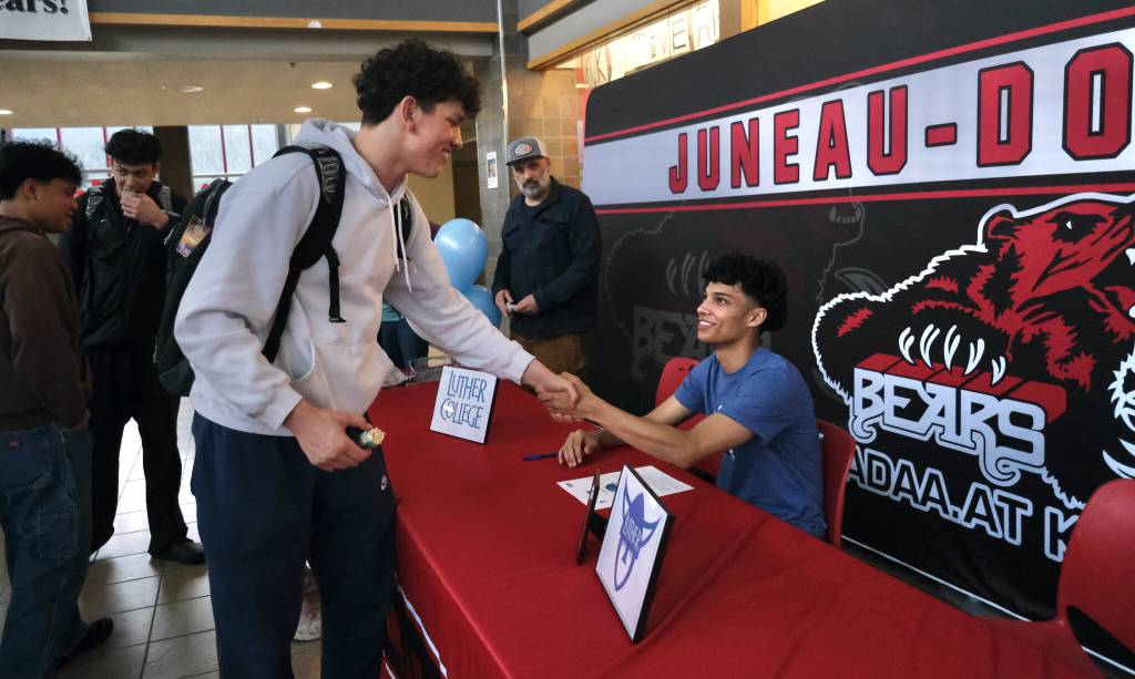 Juneau-Douglas High School: Yadaa.at Kalé sophomore Logan Carriker shakes hands with senior Pedrin Saceda-Hurt after Saceda-Hurt signed an NCAA Division III student-athlete form on Wednesday in the JDHS commons to attend Luther College in Decorah, Iowa, and play for the Norse basketball team. (Klas Stolpe/Juneau Empire)