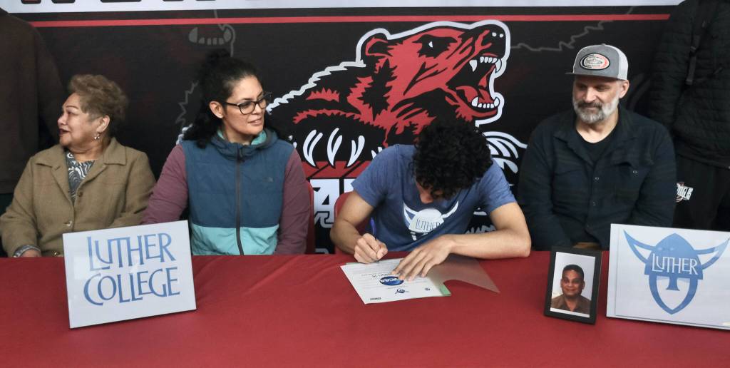 Juneau-Douglas High School: Yadaa.at Kalé senior Pedrin Saceda-Hurt signed an NCAA Division III student-athlete form on Wednesday in the JDHS commons to attend Luther College in Decorah, Iowa and play for the Norse basketball team. At left is grandmother Gethsemane Saceda, mother Nickie Saceda-Hurt and at right is father Frank Hurt. (Klas Stolpe/Juneau Empire)