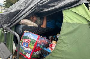 Jason Williams, a Juneau resident experiencing homelessness and suffering from multiple medical ailments, lies on a cot in a tent on the edge of a ditch on Teal Street on Saturday, May 24, 2025. (Mark Sabbatini / Juneau Empire)