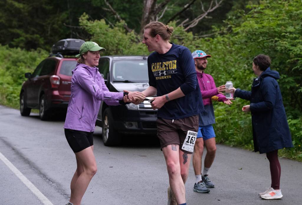 The Stragglers Therese Pokorney and Tim Mikulsi hand off at the Auke Village Recreation Area and Dimond Dogs David Fure gets refreshments during the Seacoast Relay on Sunday, June 8, 2025. (Klas Stolpe / Juneau Empire)