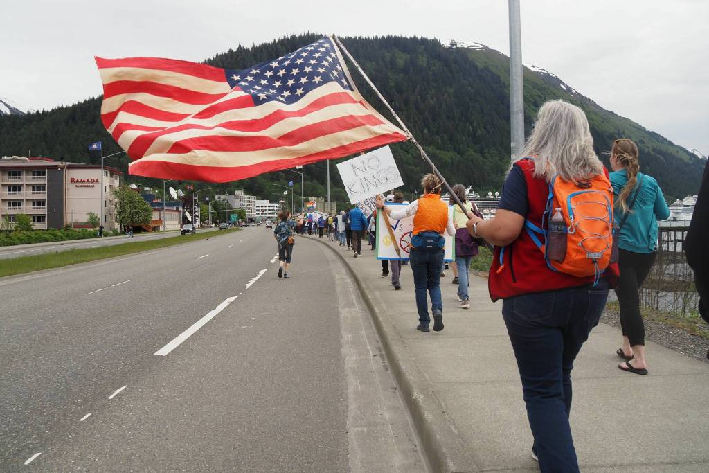 Participants in No Kings protest walk down Egan Drive waving an American flag on Saturday, June 14, 2025 (Natalie Buttner / Juneau Empire)