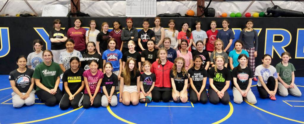 Wrestlers pose for photo at the Juneau Girls Wrestling Clinic on Wednesday at the Juneau Wrestling Center. The camp was led by 2024 Olympic Gold Medalist Amit Elor, kneeling at center front. (Klas Stolpe / Juneau Empire)