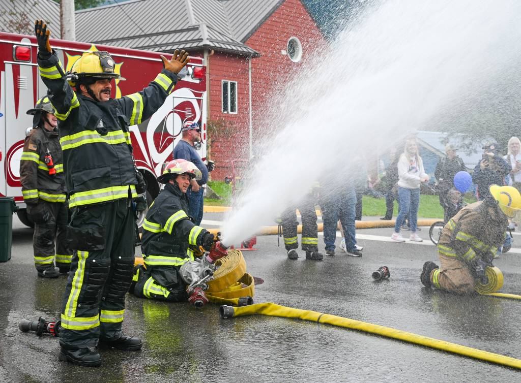 Capital City Fire/Rescue volunteer firefighter Ken Arnoldt (left) celebrates while Captain Jayme Johns (right) sprays water during the annual Olde Time Firemens Hose Race on Friday, July 4, 2025. (Jasz Garrett / Juneau Empire)