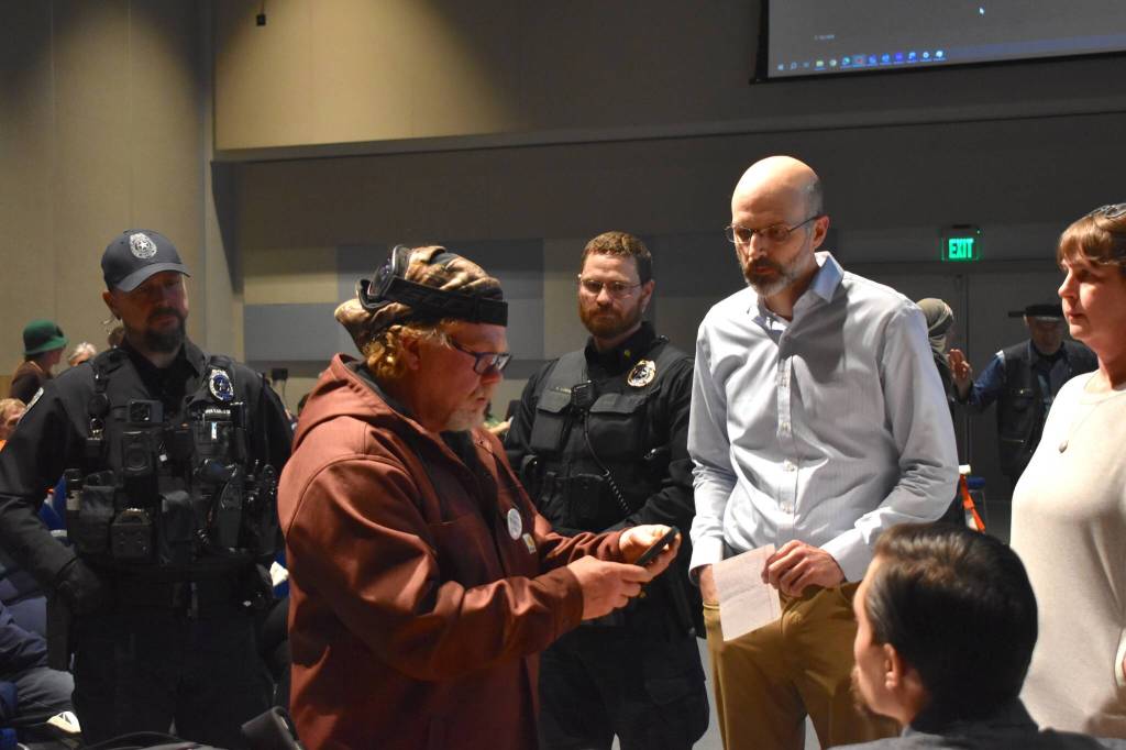Deputy City Manager Robert Barr, right, hands KC Kreger, left, a trespass letter asking him to leave the Assembly meeting on Monday, Oct. 27. (Mari Kanagy/Juneau Empire
