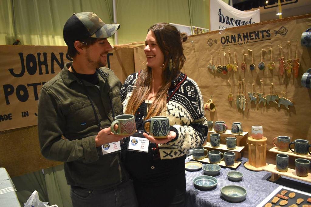 Nick Matisse and Kia Johns hold Johns mugs, two of a line of ceramic creations for sale at the Juneau Public Market on Friday, Nov. 28. (Mari Kanagy /Juneau Empire)