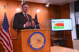 Photo by James Brooks/Alaska Beacon 
Alaska Gov. Mike Dunleavy speaks during a news conference in Juneau on Thursday, April 27, 2023. To his side is a screen displaying significant budget deficits and exhausted savings accounts if oil prices perform as expected.