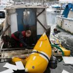 Melinos Marine Service divers Todd Hatfield, left, and Phil Sellick place absorbent cloths to soak up spilled oil after successfully re-floating a boat in Harris Harbor on Jan. 8, 2026. (Chloe Anderson for the Juneau Empire)