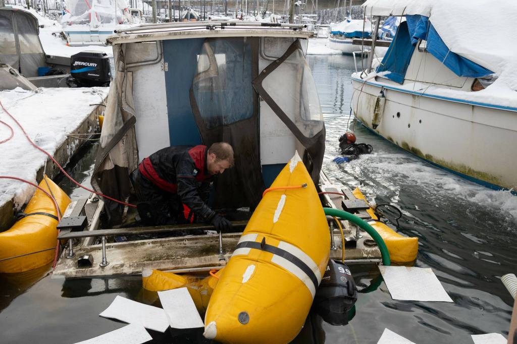 Melinos Marine Service divers Todd Hatfield, left, and Phil Sellick place absorbent cloths to soak up spilled oil after successfully re-floating a boat in Harris Harbor on Jan. 8, 2026. (Chloe Anderson for the Juneau Empire)