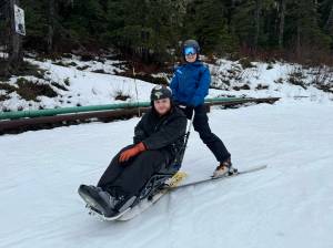 ORCA Adaptive Snowsports Program staff member Izzy Barnwell shows a man how to use the bi-ski. (SAIL courtesy photo)