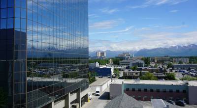 Part of the Anchorage skyline is reflected in the south-facing windows of downtowns Robert B. Atwood Building on June 17, 2026. Anchorage, Alaskas biggest city, had a cost of living that was 25.5% above the national urban average in 2025, according to the Alaska Department of Labor and Worforce Development. (Photo by Yereth Rosen/Alaska Beacon)
